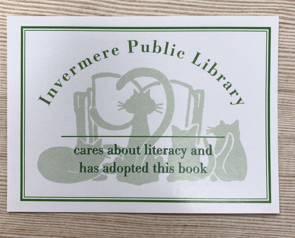 Picture of an Invermere Public Library book plate. The bookplate is white with a green border. There is an image of 4 cats reading a book, faded as the background. Text over that that read "Invermere Public Library" and then a blank line to add someone's name and sentence below that says "cares about literacy and has adopted this book."